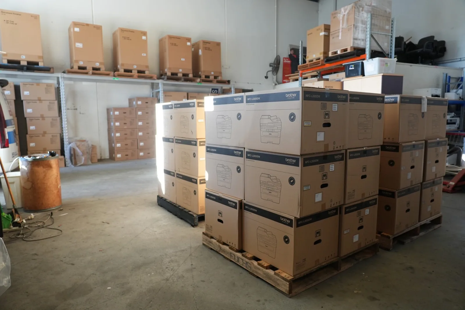 Pallets stacked with boxed Brother MFC-L2820DW printers, with further pallets of document finishers and paper feeders on the racking behind